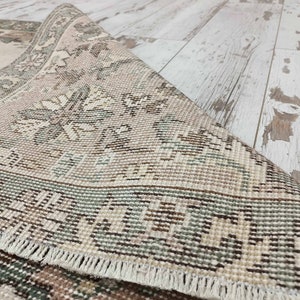 May include: Close-up of a beige and green patterned rug with a fringed border. The rug is woven with a detailed floral design.