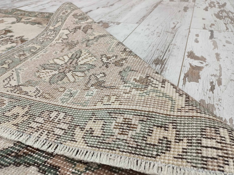 May include: Close-up of a beige and green patterned rug with a fringed border. The rug is woven with a detailed floral design.