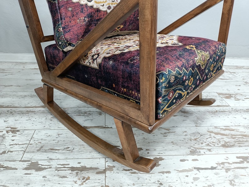 May include: A wooden rocking chair with a patterned cushion. The chair has a dark wood frame and a seat cushion with a burgundy, cream, and navy pattern. The chair's design includes a slatted back and curved rockers.