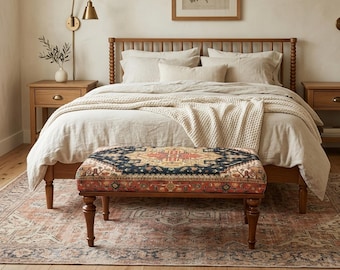 Könnte beinhalten: Ein Schlafzimmer mit einem hölzernen Bettrahmen, neutraler Bettwäsche und einer gemusterten Bank. Die Bank hat ein rotes, blaues und goldenes Design. Ein Teppich mit ähnlichem Farbschema liegt auf dem Boden. Warme Atmosphäre.