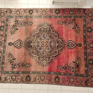 May include: A vintage Persian rug with a faded pink background and intricate floral patterns in shades of brown, green, and black. The rug has a border with a repeating design.