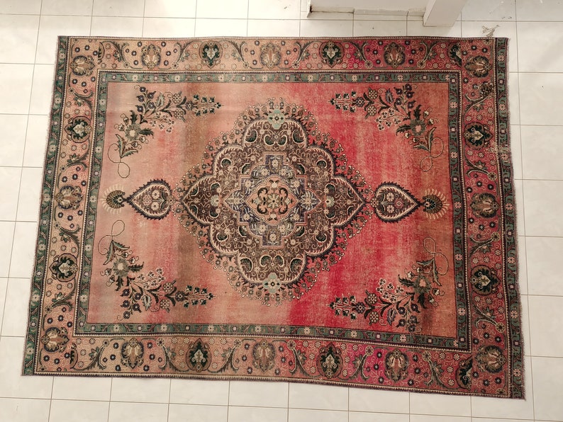 May include: A vintage Persian rug with a faded pink background and intricate floral patterns in shades of brown, green, and black. The rug has a border with a repeating design.