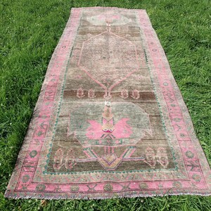 May include: A vintage pink and brown rug with a geometric pattern. The rug has a fringed edge and is laid out on a green grassy surface.
