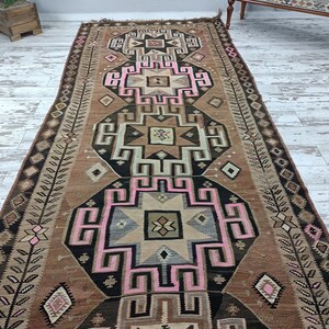 May include: A vintage Turkish rug with a geometric pattern in shades of brown, pink, and black. The rug has a traditional design with intricate details and a faded, worn look.