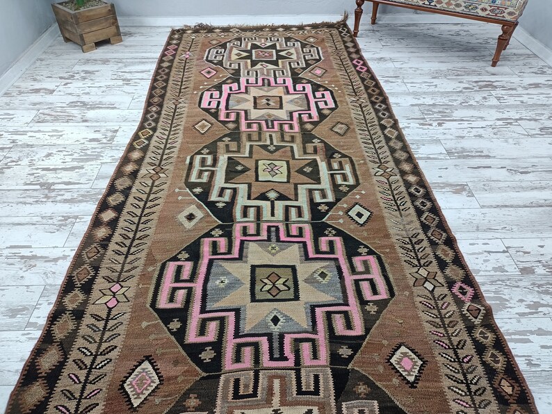 May include: A vintage Turkish rug with a geometric pattern in shades of brown, pink, and black. The rug has a traditional design with intricate details and a faded, worn look.