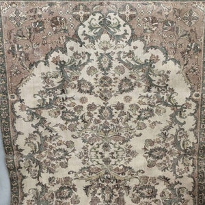 May include: A vintage rug with a cream background and intricate floral patterns in shades of brown, green, and pink. The rug has a border with a geometric design.