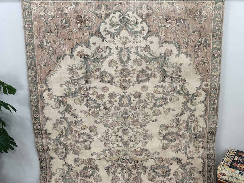 May include: A vintage rug with a cream background and intricate floral patterns in shades of brown, green, and pink. The rug has a border with a geometric design.