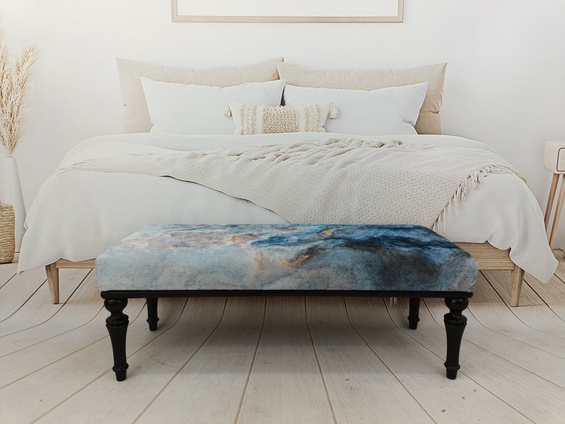 Puede incluir: Un banco con estampado azul y gris con patas de madera negra. El banco est&aacute; en un dormitorio con una cama blanca y una manta blanca.