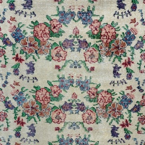 May include: A cream-colored rug with a floral pattern in shades of pink, blue, green, and brown. The rug has a green border.