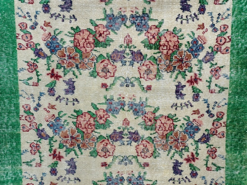 May include: A cream-colored rug with a floral pattern in shades of pink, blue, green, and brown. The rug has a green border.