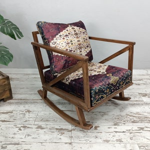 May include: Wooden rocking chair with a patterned cushion. The chair has a dark wood frame and a cushion with a burgundy, cream, and navy pattern. The chair is designed with a classic rocking base.