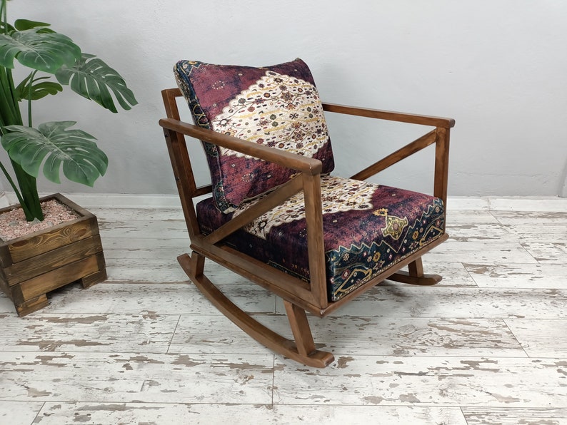 May include: Wooden rocking chair with a patterned cushion. The chair has a dark wood frame and a cushion with a burgundy, cream, and navy pattern. The chair is designed with a classic rocking base.
