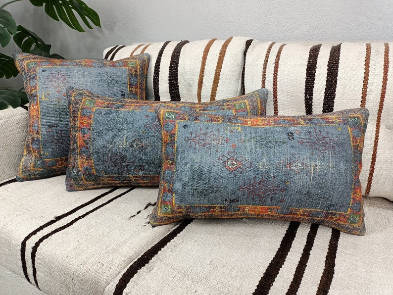 Op de afbeelding: Vier decoratieve kussens met een blauwe achtergrond en ingewikkelde oranje, rode en groene patronen. De kussens zijn gerangschikt op een witte en bruine gestreepte bank.