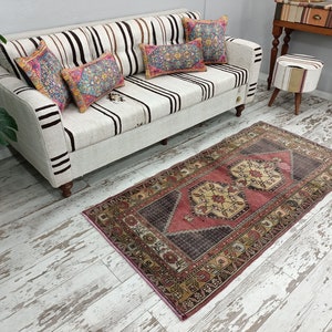 May include: A white and brown striped sofa with three colorful throw pillows. The sofa is sitting on a whitewashed wood floor with a pink and brown patterned rug in front of it.
