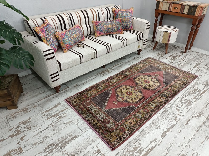 May include: A white and brown striped sofa with three colorful throw pillows. The sofa is sitting on a whitewashed wood floor with a pink and brown patterned rug in front of it.