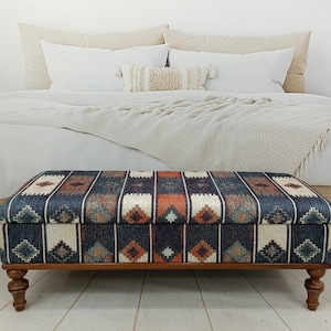 May include: A rectangular storage ottoman with a dark blue, orange and white geometric patterned fabric top and wooden legs.