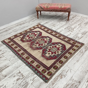May include: A cream-colored rug with a red, green, and blue geometric pattern. The rug has a border with a repeating pattern of flowers and leaves.