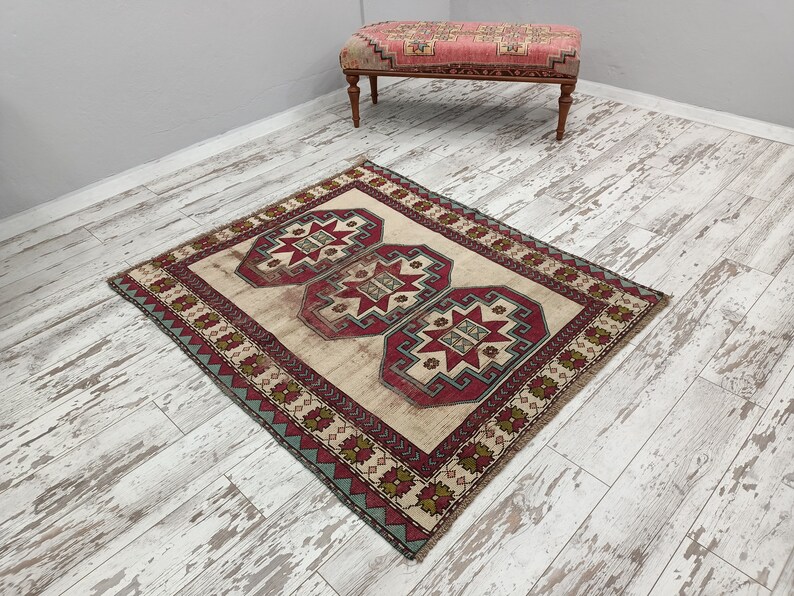 May include: A cream-colored rug with a red, green, and blue geometric pattern. The rug has a border with a repeating pattern of flowers and leaves.