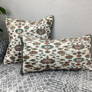 Könnte beinhalten: Zwei dekorative Kissen mit weißem Hintergrund und einem floralen Muster in Grün-, Orange- und Brauntönen.