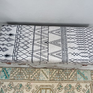 May include: A white and black patterned storage ottoman with a geometric design. The ottoman is sitting on a rug with a similar pattern.
