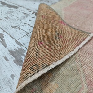 May include: Close-up of the back side of a pink and beige rug with a fringed border. The rug is rolled up and the back side is visible, showing the woven texture and a brown colour.