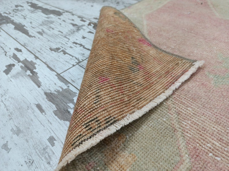 May include: Close-up of the back side of a pink and beige rug with a fringed border. The rug is rolled up and the back side is visible, showing the woven texture and a brown colour.