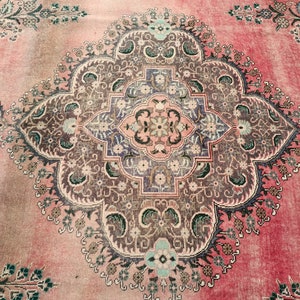 May include: A vintage rug with a pink background and intricate floral patterns in shades of brown, green, and blue. The rug features a central medallion with a geometric design.