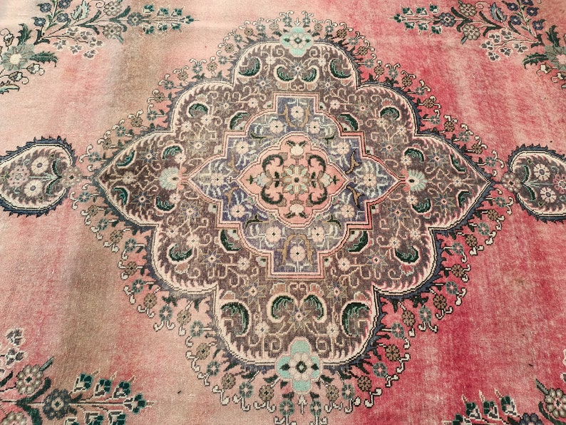 May include: A vintage rug with a pink background and intricate floral patterns in shades of brown, green, and blue. The rug features a central medallion with a geometric design.