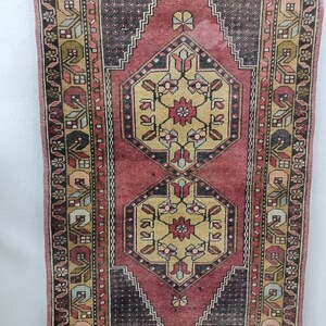 May include: A vintage Turkish runner rug with a red, cream, and black geometric pattern. The rug has a faded, distressed look and features intricate floral designs.