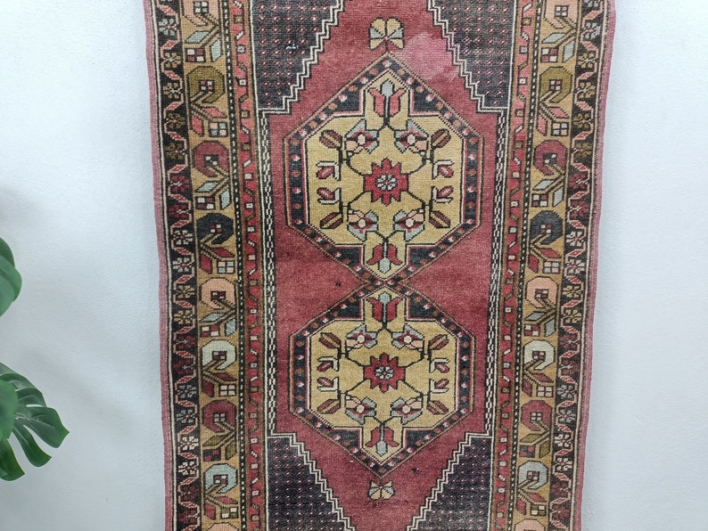 May include: A vintage Turkish runner rug with a red, cream, and black geometric pattern. The rug has a faded, distressed look and features intricate floral designs.