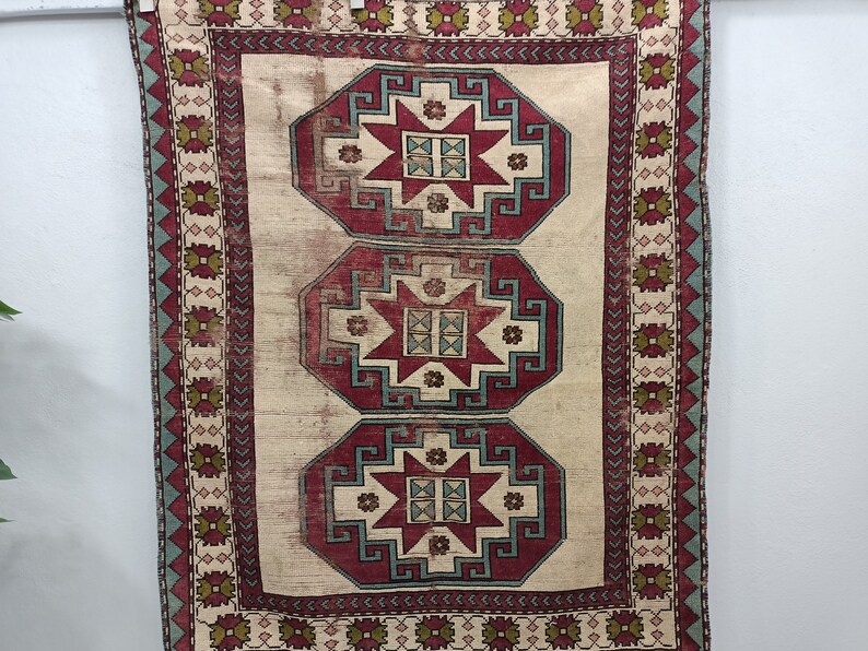 May include: A vintage rug with a cream background and three red, blue, and green octagonal medallions with star-shaped designs. The rug has a border with a repeating pattern of green, red, and blue.