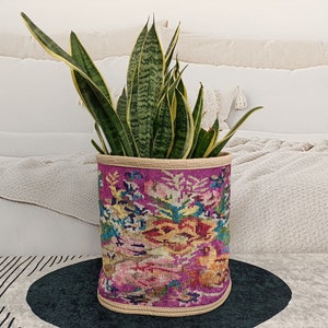 Puede incluir: Una planta de serpiente en maceta con hojas verdes y amarillas en una maceta de tela con estampado rosa y crema.