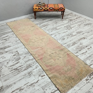 May include: A long, rectangular runner rug with a faded pink and cream colour scheme. The rug has a traditional floral pattern and is laid out on a whitewashed wood floor.
