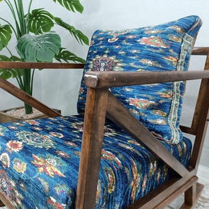 a wooden rocking chair with a blue and white patterned cushion, placed in front of a potted plant.
