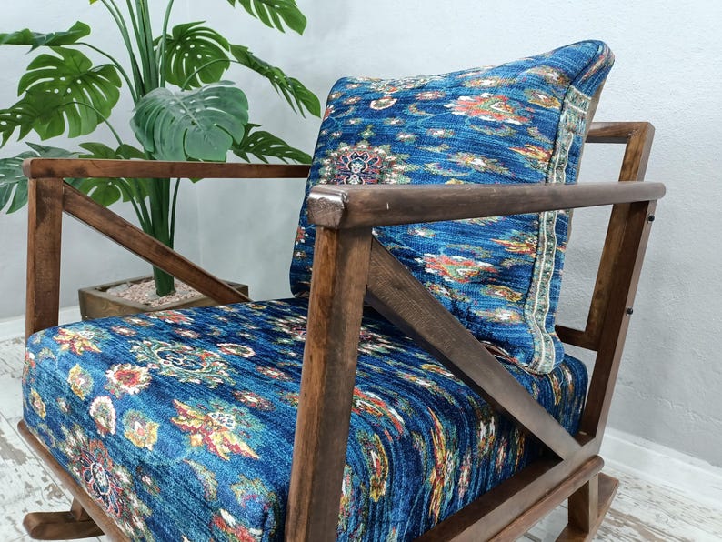 a wooden rocking chair with a blue and white patterned cushion, placed in front of a potted plant.