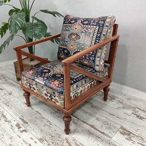 Puede incluir: Un sill&oacute;n de madera con un coj&iacute;n y respaldo de tela estampada. La silla tiene un marco y patas de madera oscura. La tela es una mezcla de azul, rojo y blanco.