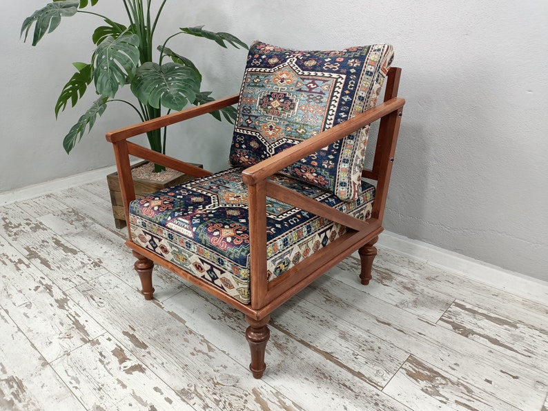 Puede incluir: Un sill&oacute;n de madera con un coj&iacute;n y respaldo de tela estampada. La silla tiene un marco y patas de madera oscura. La tela es una mezcla de azul, rojo y blanco.