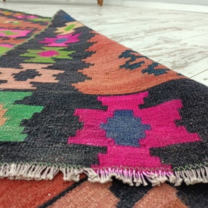 Puede incluir: Primer plano de una alfombra tejida colorida con fondo negro y patrones geom&eacute;tricos. La alfombra tiene un borde de flecos y est&aacute; hecha de lana.