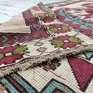 May include: Close-up of a beige, red, green, and blue patterned rug with a fringe border.