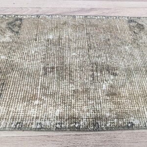 May include: A close-up of a light brown and white woven rug with a distressed look. The rug has a subtle pattern and a frayed edge.
