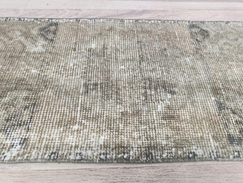 May include: A close-up of a light brown and white woven rug with a distressed look. The rug has a subtle pattern and a frayed edge.