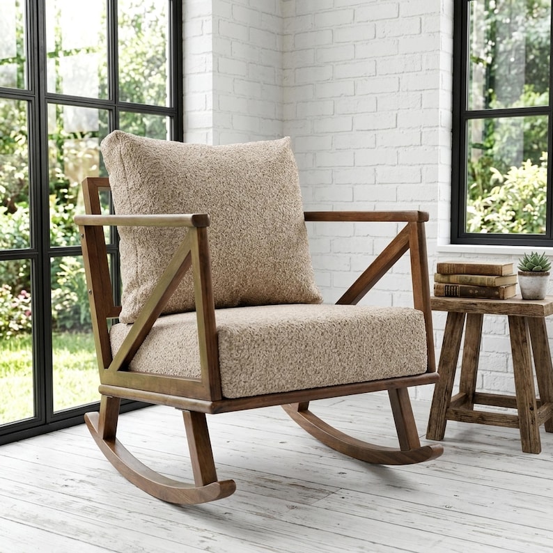 A wooden rocking chair with a beige cushion sits in a room with large windows overlooking a lush garden.