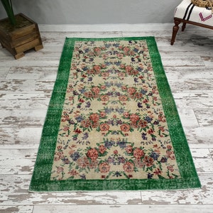 May include: A vintage floral rug with a cream background and a green border. The rug features a repeating pattern of pink, red, and purple flowers.