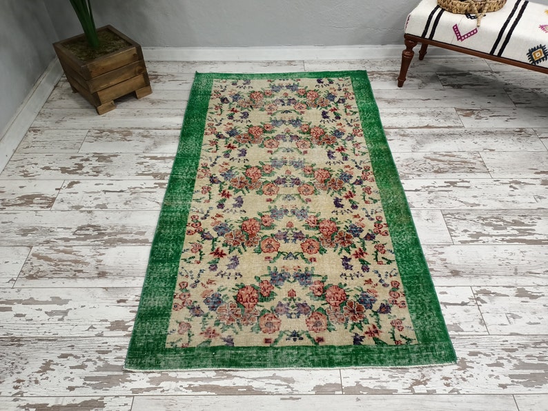 May include: A vintage floral rug with a cream background and a green border. The rug features a repeating pattern of pink, red, and purple flowers.
