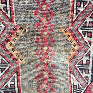 May include: Close-up of a red, black, and white patterned rug with a geometric design. The rug has a worn, vintage look.