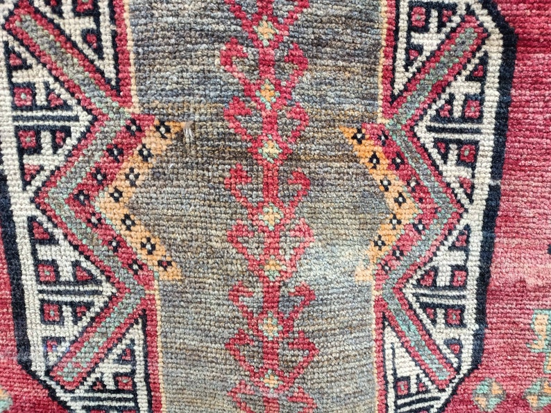 May include: Close-up of a red, black, and white patterned rug with a geometric design. The rug has a worn, vintage look.
