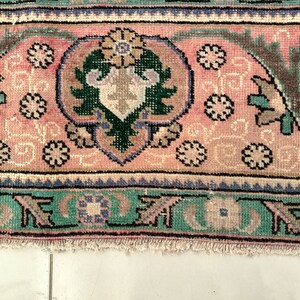 May include: Close-up of a pink and green patterned rug with a fringed edge. The rug features a floral design with intricate details.
