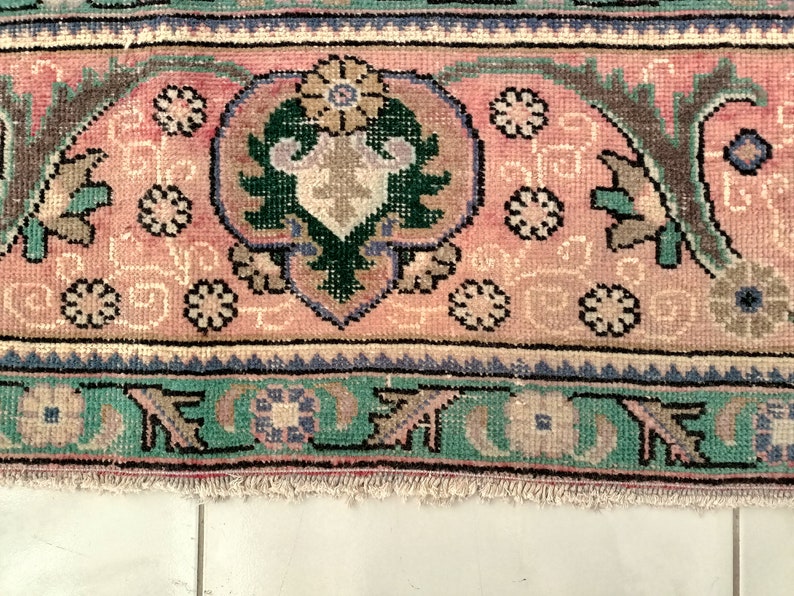May include: Close-up of a pink and green patterned rug with a fringed edge. The rug features a floral design with intricate details.