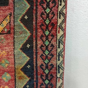 May include: Close-up of a red, blue, and green patterned rug with a fringe edge. The rug has a traditional design with geometric shapes and floral motifs.