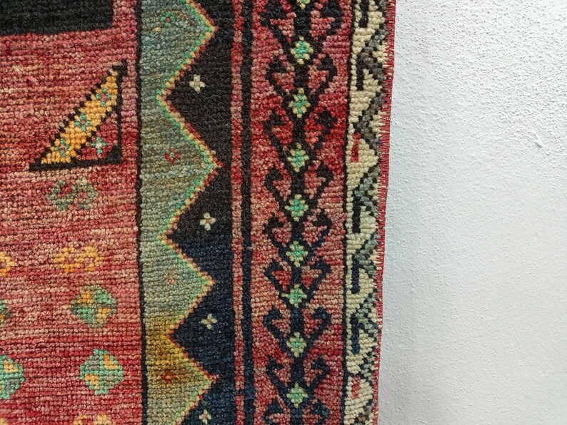 May include: Close-up of a red, blue, and green patterned rug with a fringe edge. The rug has a traditional design with geometric shapes and floral motifs.